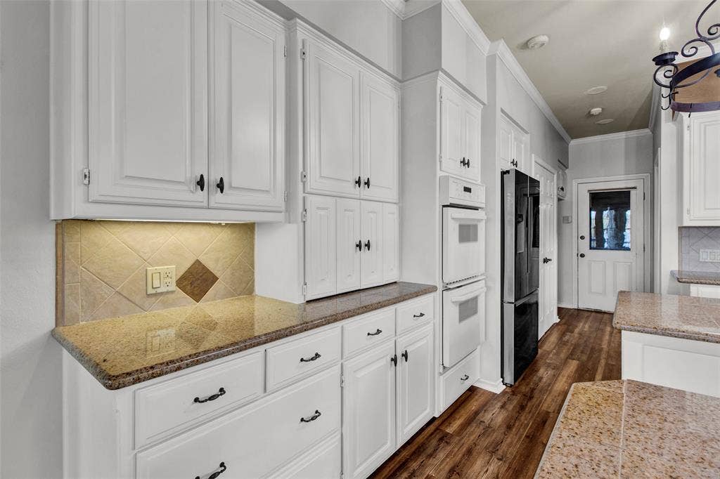 1551 E Tanglewood, Hideaway, TX 75771 White cabinetry with dark hardware, granite countertops, tile backsplash, built-in double ovens, and wood-finish flooring