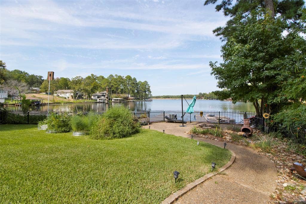 1551 E Tanglewood, Hideaway, TX 75771 Lakeside property featuring a manicured lawn, a winding stone-edged pathway, a black wrought-iron fence, and direct lake access