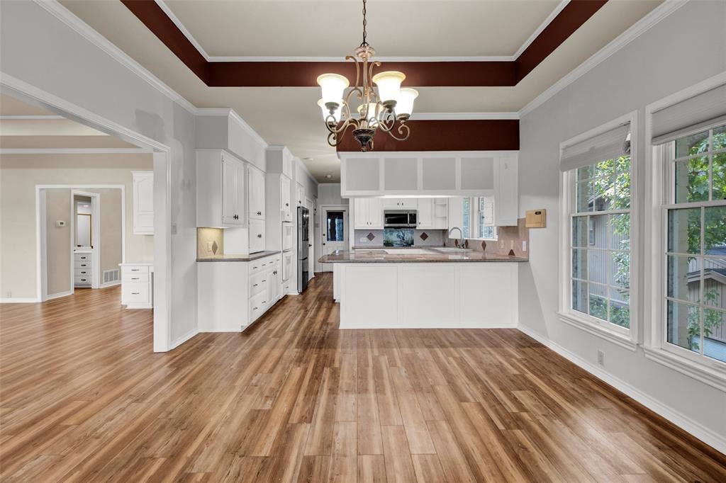 1551 E Tanglewood, Hideaway, TX 75771 Spacious room featuring wood-finish flooring, a coffered ceiling, and a kitchen area with white cabinetry, stainless steel appliances, and a tiled backsplash