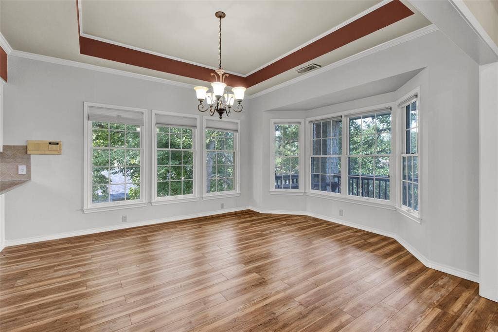 1551 E Tanglewood, Hideaway, TX 75771 Recessed ceiling detail with a decorative chandelier, multiple windows with grid patterns, a bay window feature, and wood-finish flooring