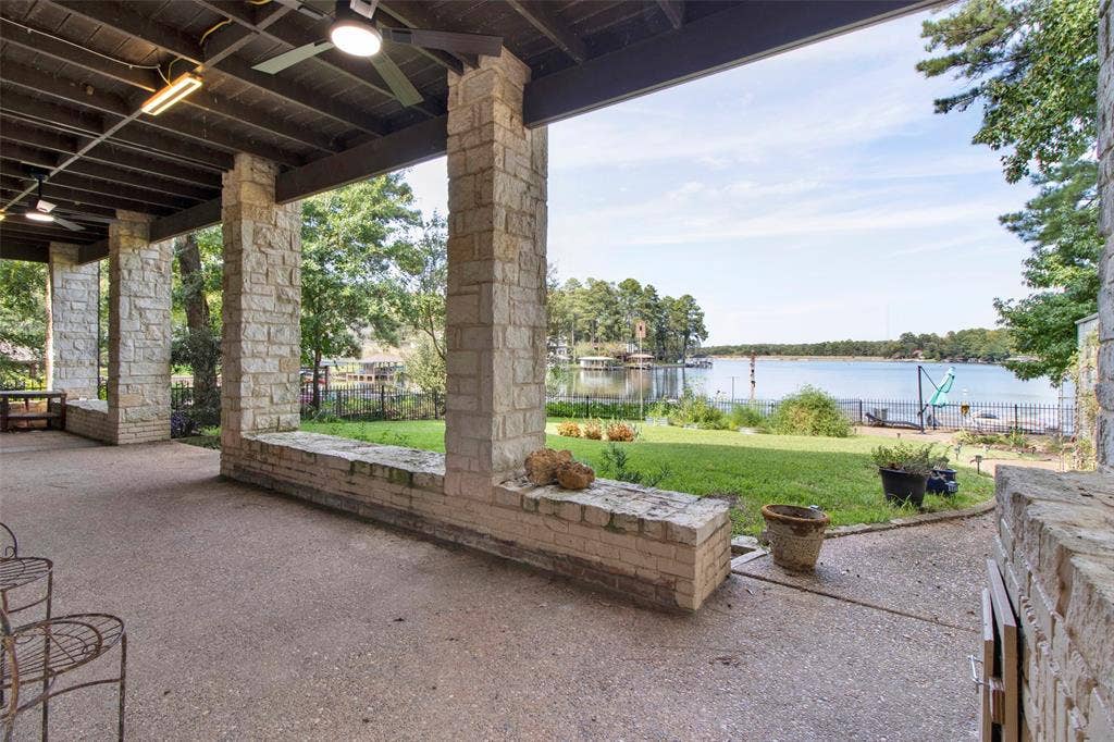 1551 E Tanglewood, Hideaway, TX 75771 Covered patio with stone pillars and a ceiling fan, overlooking a spacious lawn and a body of water