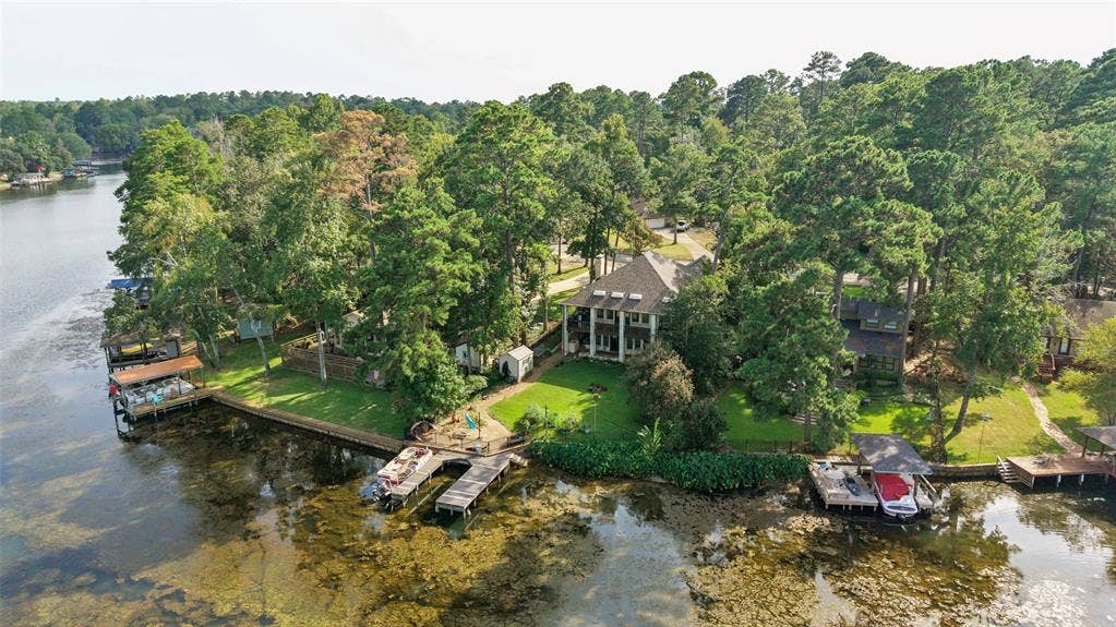 1551 E Tanglewood, Hideaway, TX 75771 Waterfront property featuring a private boat dock, a covered boat slip, mature trees, a manicured lawn, and a multi-story residence with a columned front porch