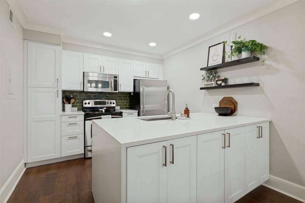 5934 Sandhurst Lane, #208, Dallas, TX 75206 White shaker cabinetry paired with stainless steel appliances, a center island featuring an undermount sink, recessed lighting, and wood-finish flooring