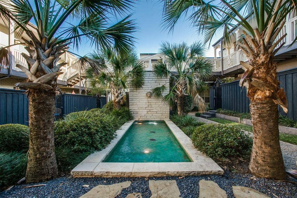 5934 Sandhurst Lane, #208, Dallas, TX 75206 Landscaped courtyard featuring a rectangular water feature with a stone surround, stone accent wall, decorative gravel, and established palm trees