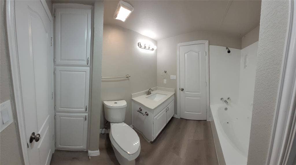 1501 Cedar Elm Drive, #102, Euless, TX 76039 White cabinetry with integrated storage, single vanity with countertop, light wood-finish flooring, toilet, and bathtub with shower