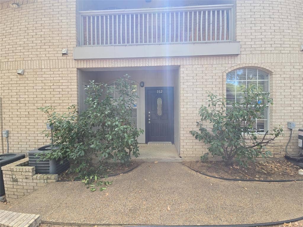 1501 Cedar Elm Drive, #102, Euless, TX 76039 Brick exterior featuring an arched window, a privacy balcony, and a dark entry door with decorative glass