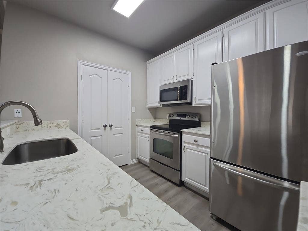 1501 Cedar Elm Drive, #102, Euless, TX 76039 Kitchen featuring white cabinetry, light-toned countertops, stainless steel appliances, and wood-finish flooring