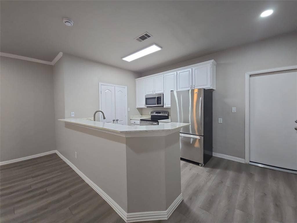 1501 Cedar Elm Drive, #102, Euless, TX 76039 Kitchen featuring white cabinetry, stainless steel appliances, a breakfast bar with a solid surface countertop, and wood-finish flooring