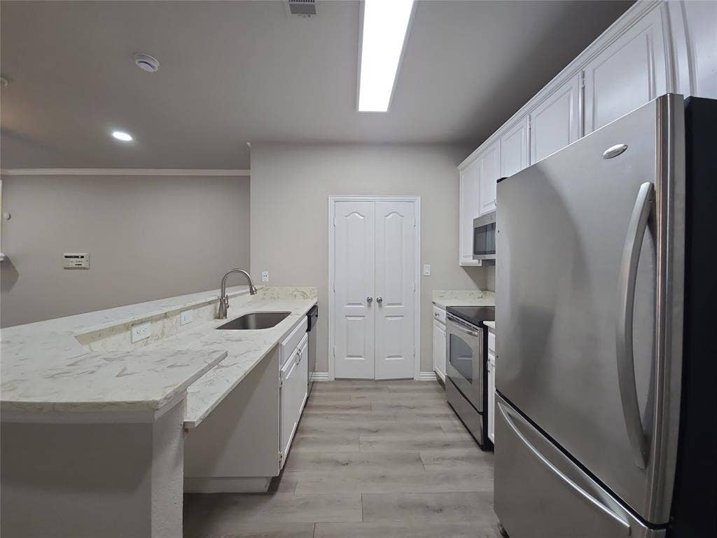 1501 Cedar Elm Drive, #102, Euless, TX 76039 Kitchen featuring wood-finish flooring, white cabinetry, integrated stainless steel appliances, and a double-basin sink with a gooseneck faucet