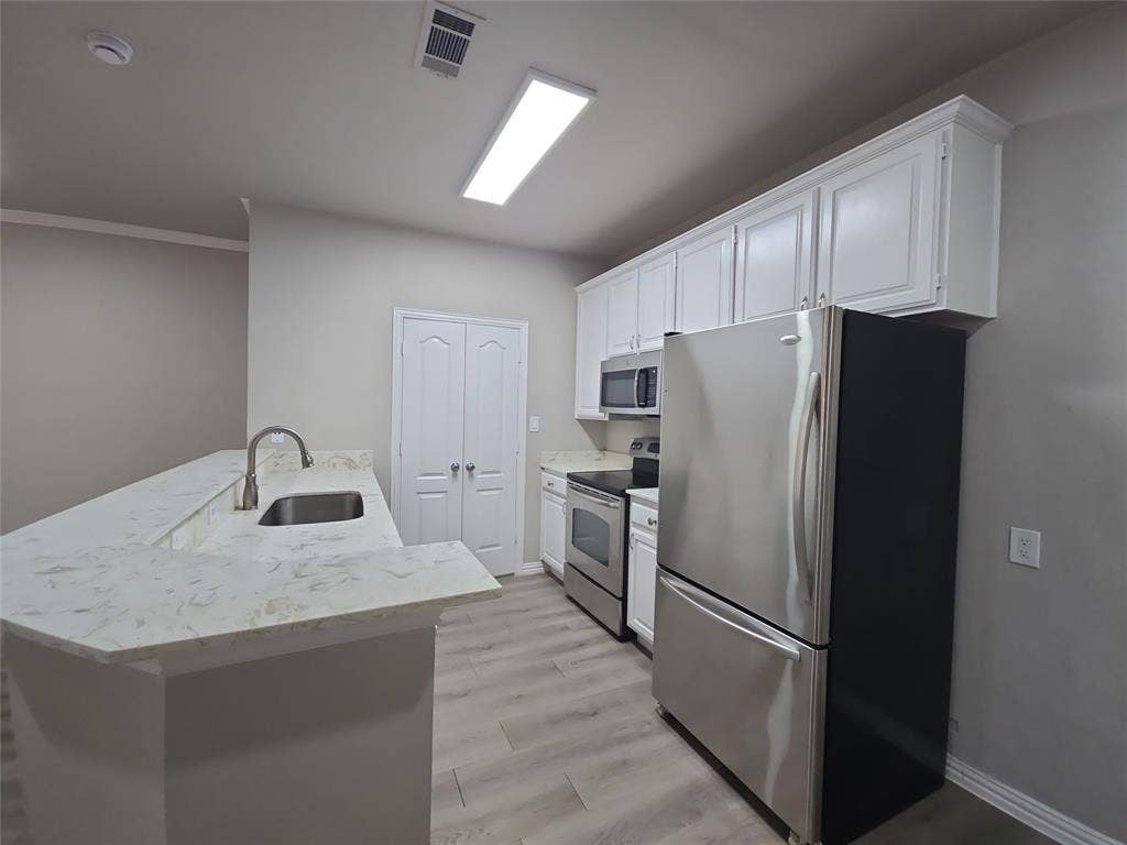 1501 Cedar Elm Drive, #102, Euless, TX 76039 Kitchen featuring white cabinetry, stainless steel appliances, light-toned countertops, and wood-finish flooring