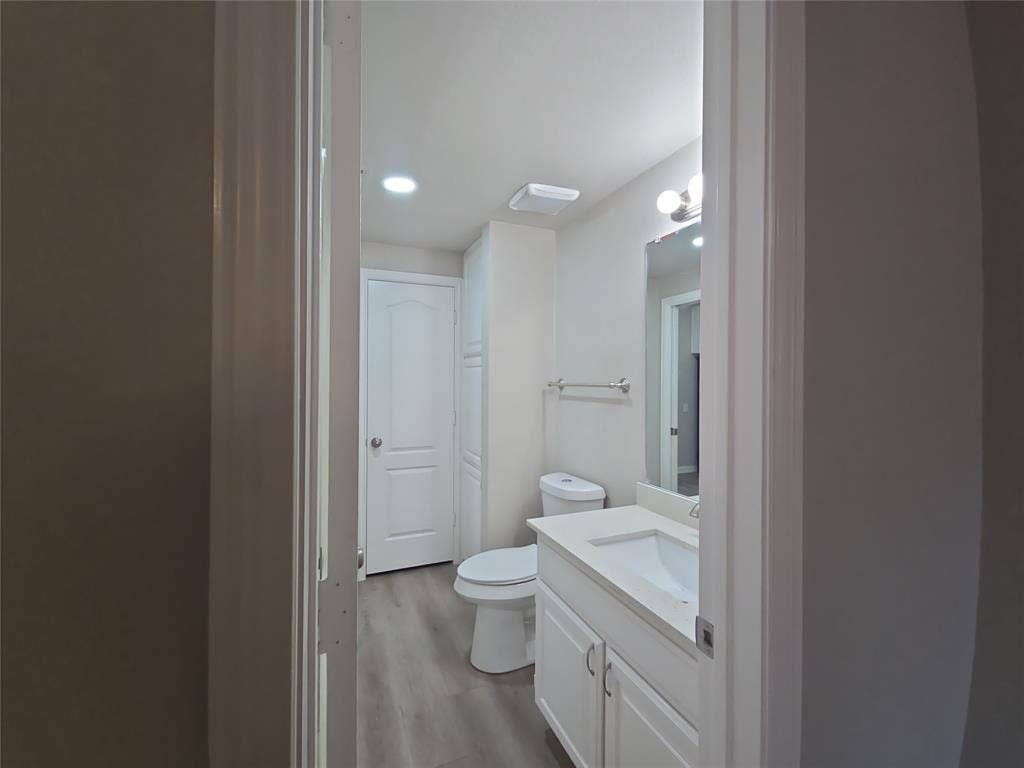 1501 Cedar Elm Drive, #102, Euless, TX 76039 Bathroom featuring a white vanity with integrated sink, white cabinetry, wall-mounted mirror, and wood-finish flooring