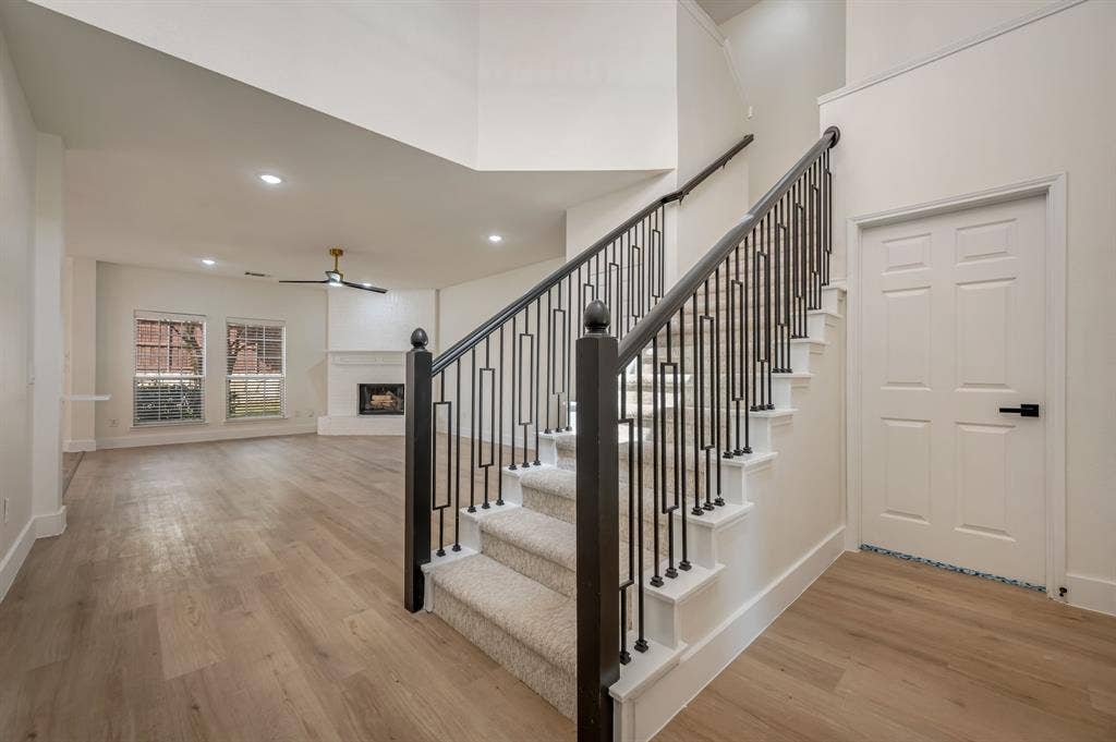 7904 Blacktail Trail, McKinney, TX 75070 Luxury Vinyl Plank flooring, staircase with wrought iron balusters, carpeted stair treads, ceiling fan with integrated lighting, and a fireplace with a white mantel