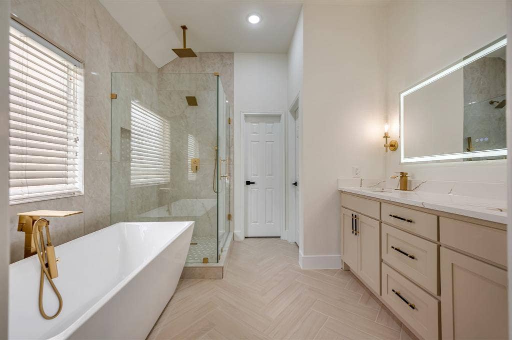 7904 Blacktail Trail, McKinney, TX 75070 Freestanding soaking tub with gold-tone fixtures, walk-in shower with glass enclosure, dual vanity with undermount sinks, illuminated mirror, and herringbone-patterned tile flooring