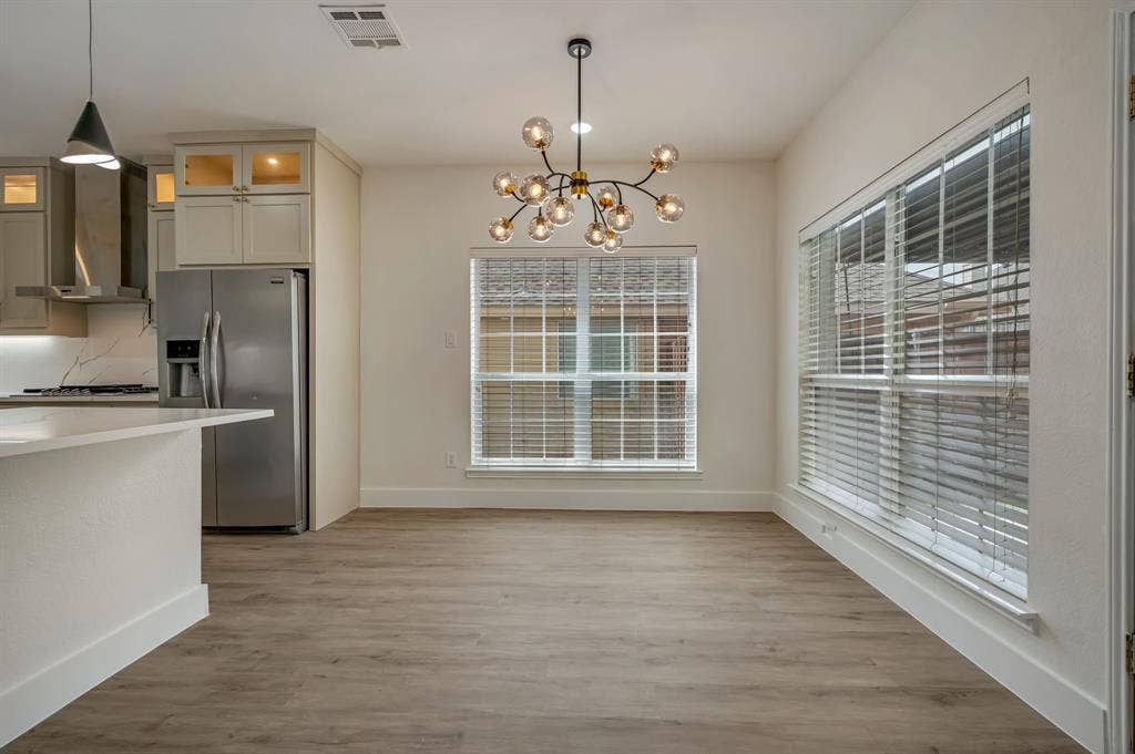 7904 Blacktail Trail, McKinney, TX 75070 Open-concept living space featuring Luxury Vinyl Plank flooring, a contemporary chandelier, large windows with blinds, and a kitchen with stainless steel appliances and light-toned cabinetry