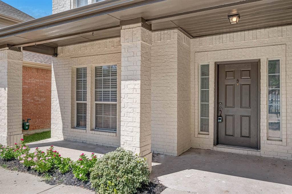7904 Blacktail Trail, McKinney, TX 75070 Cream-colored brick exterior with a covered porch, recessed lighting, and a dark paneled entry door