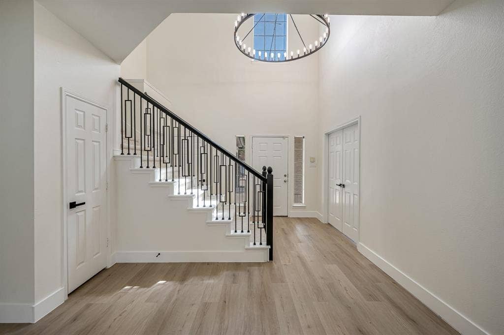 7904 Blacktail Trail, McKinney, TX 75070 Grand foyer featuring Luxury Vinyl Plank flooring, a contemporary chandelier, and a prominent staircase with decorative iron railings