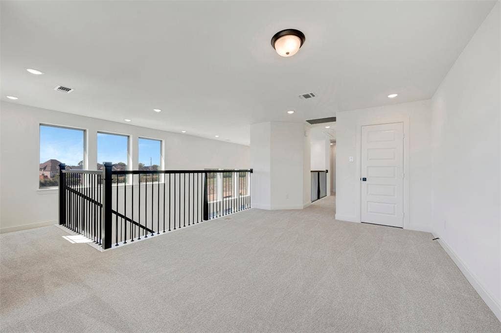 1616 Compass Heights, Mesquite, TX 75181 Spacious loft featuring light-toned carpeting, multiple windows, a black metal railing, a panel door, and recessed lighting