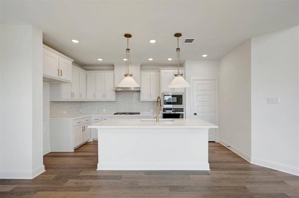 1616 Compass Heights, Mesquite, TX 75181 Modern kitchen featuring white shaker cabinetry, an expansive center island, integrated stainless steel appliances, a tile backsplash, and wood-finish flooring