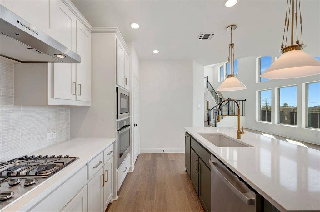 1616 Compass Heights, Mesquite, TX 75181 Kitchen featuring white shaker cabinetry, stainless steel appliances, wood-finish flooring, a center island with a sink, and pendant lighting