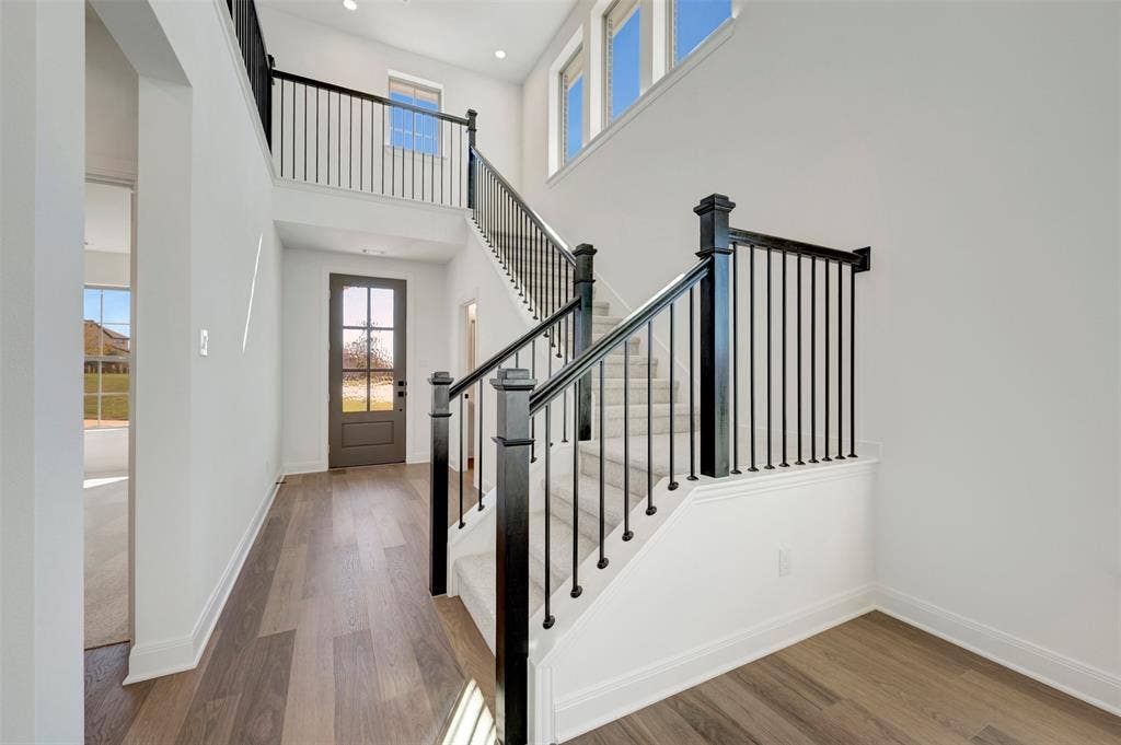1616 Compass Heights, Mesquite, TX 75181 Entryway featuring high ceilings, wood-finish flooring, a contemporary staircase with dark wood newel posts and black metal balusters, and a panel-glass entry door