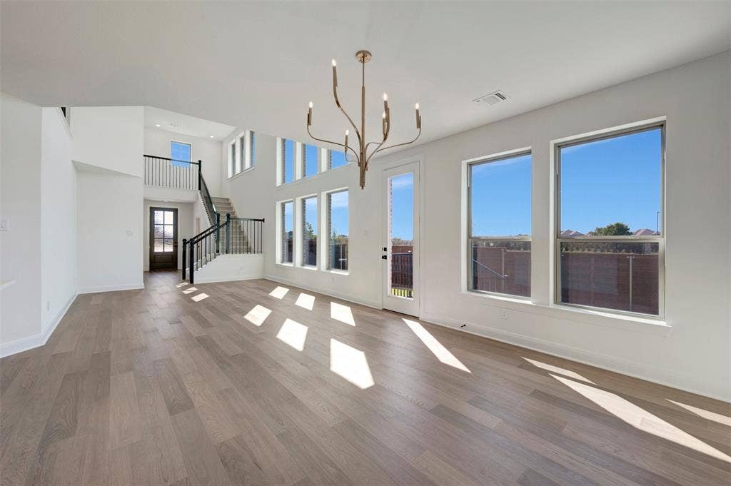 1616 Compass Heights, Mesquite, TX 75181 Open-concept living space featuring wood-finish flooring, a two-story ceiling, a modern chandelier, a prominent staircase with metal railings, and multiple large windows