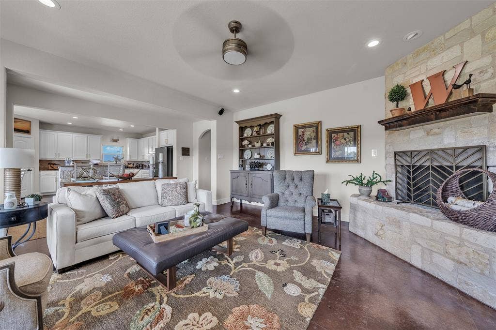 Stone-faced fireplace with a wood mantel, dark wood-finish flooring, recessed lighting, and a ceiling fan with integrated lighting