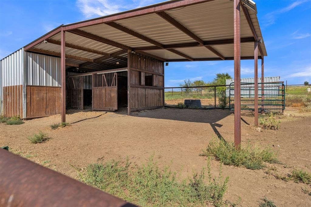 Metal barn structure with an extended corrugated metal roof overhang, featuring wood-finish stalls and an open-air covered area