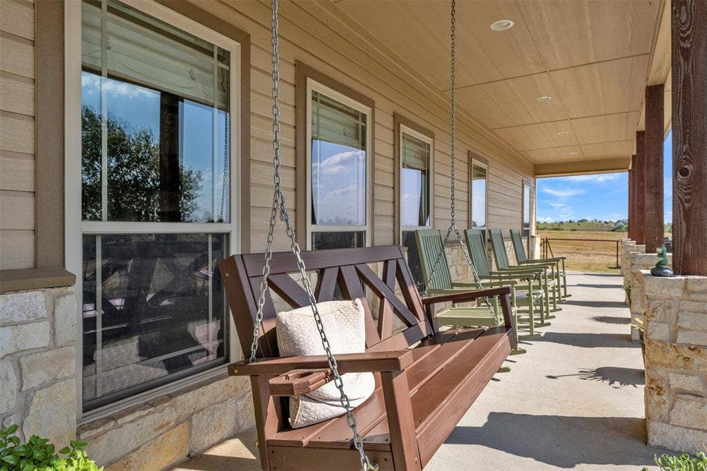Covered porch featuring a wood-slat ceiling with recessed lighting, stone column bases, and a concrete floor