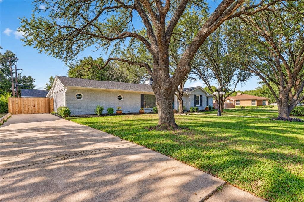 1204 Loma Alta Place, Cleburne, TX 76033 Expansive front yard with mature trees, a concrete driveway, and a wood privacy fence