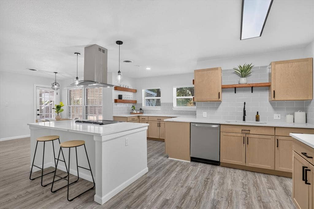 1204 Loma Alta Place, Cleburne, TX 76033 Kitchen featuring wood-finish cabinetry, light-toned countertops, a stainless steel range hood, light gray subway tile backsplash, and wood-finish flooring