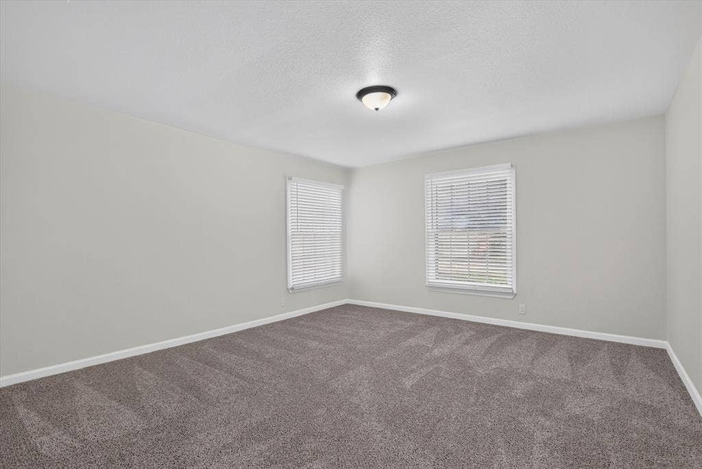 1204 Loma Alta Place, Cleburne, TX 76033 Plush grey carpeting, two windows with blinds, light neutral wall paint, and a semi-flush mount ceiling light