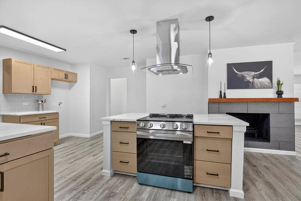 1204 Loma Alta Place, Cleburne, TX 76033 Kitchen island with built-in stainless steel range, stainless steel range hood, light wood-finish cabinetry, white countertops, and wood-finish flooring