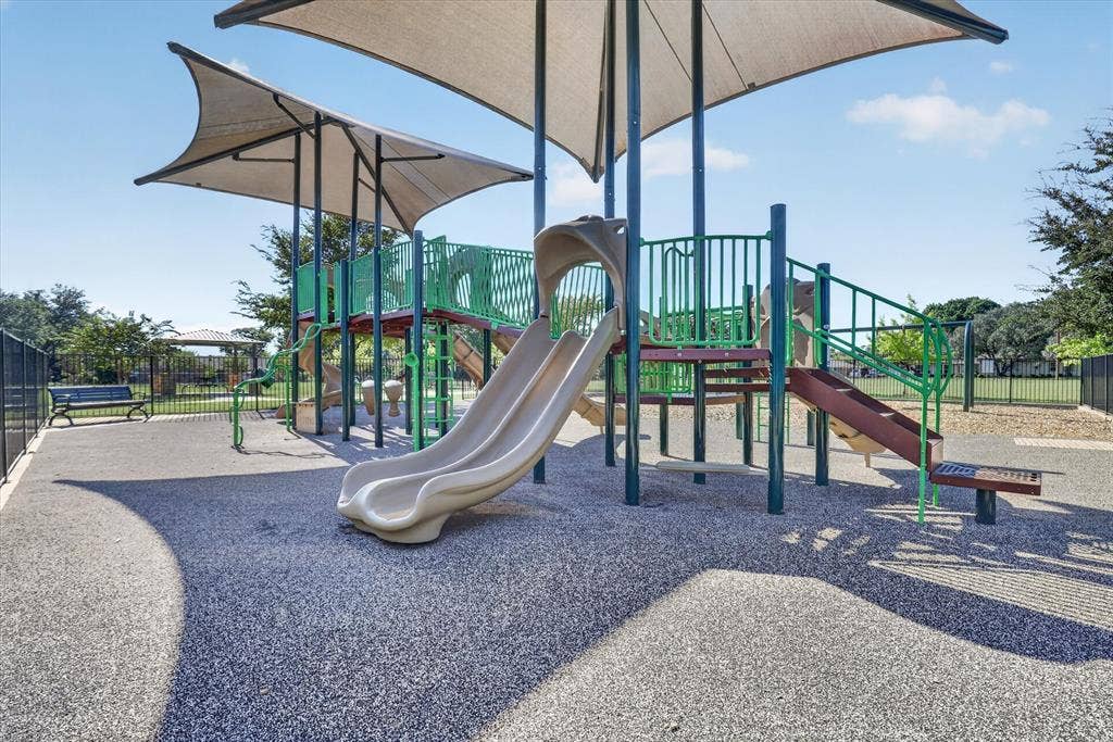 1204 Loma Alta Place, Cleburne, TX 76033 Playground featuring a tan shade structure, multi-level play equipment with slides, a soft-surface ground cover, and surrounding black fencing