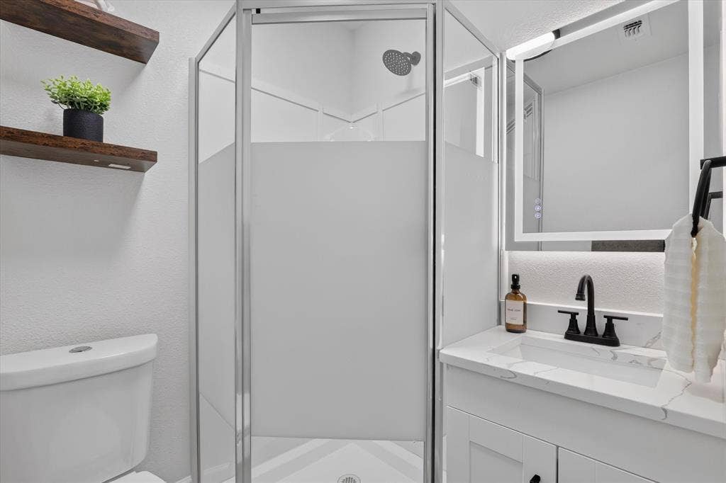1204 Loma Alta Place, Cleburne, TX 76033 Shower enclosure with frosted glass, showerhead, vanity with integrated sink, black-finish faucet, and an illuminated medicine cabinet