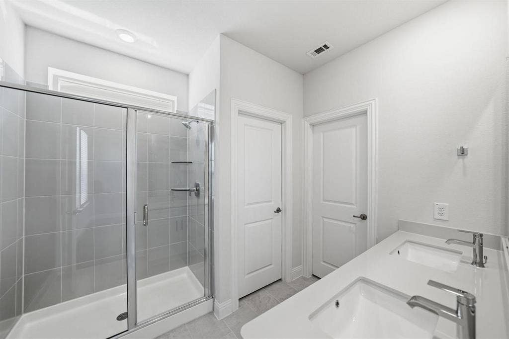 4532 Community Court, Plano, TX 75024 Dual sinks with chrome fixtures, a spacious walk-in shower with glass enclosure, light gray tiled shower walls, and white countertops