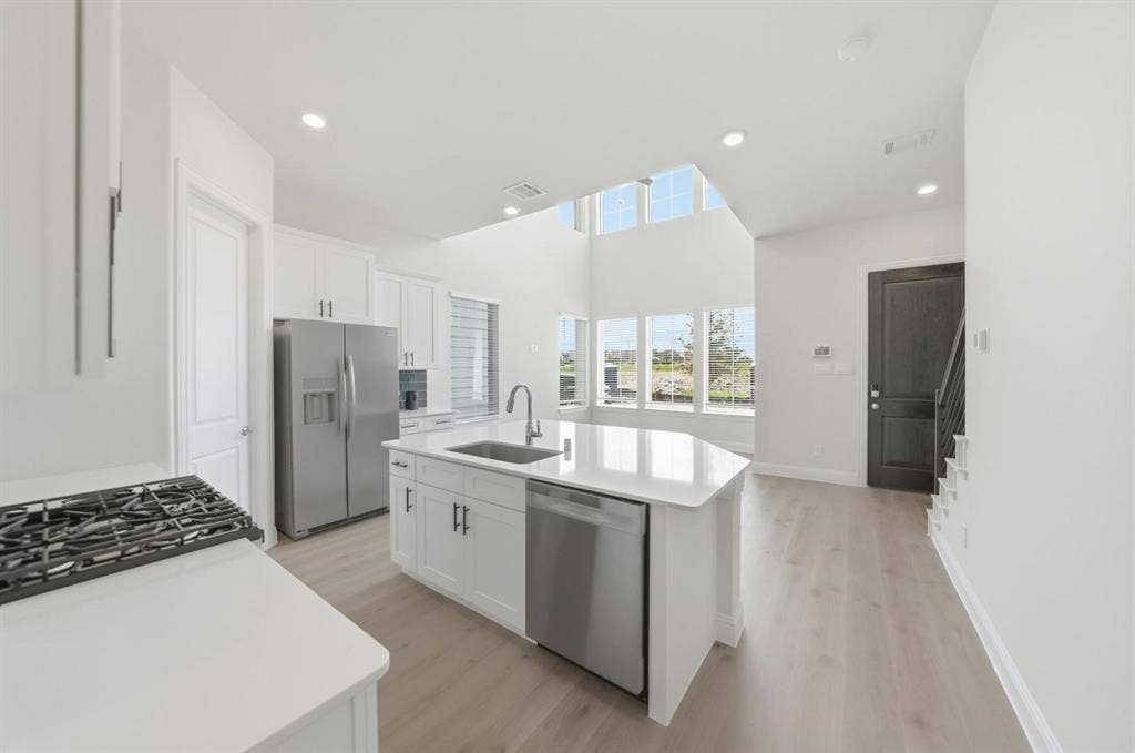 4532 Community Court, Plano, TX 75024 Modern kitchen featuring white cabinetry, stainless steel appliances, a center island with sink, and light wood-finish flooring