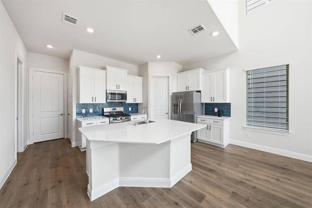 4532 Community Court, Plano, TX 75024 Kitchen featuring wood-finish flooring, white cabinetry with silver hardware, a stainless steel gas range, a stainless steel microwave, and a center island with a white countertop