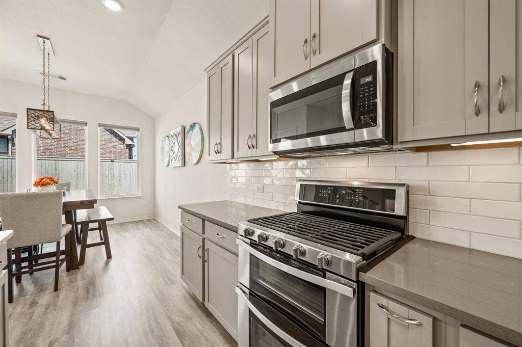 2900 Peekaboo Lane, Northlake, TX 76247 Contemporary kitchen featuring stainless steel appliances, grey cabinetry, light-toned quartz countertops, subway tile backsplash, and LTV flooring