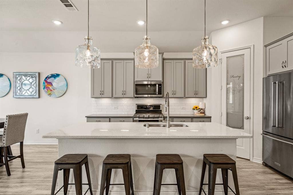 2900 Peekaboo Lane, Northlake, TX 76247 Kitchen featuring a wonderfully sized island with quartz countertop, stainless steel appliances, grey cabinetry, LTV flooring and fabulous pendant lighting to make your kitchen even more spectacular!