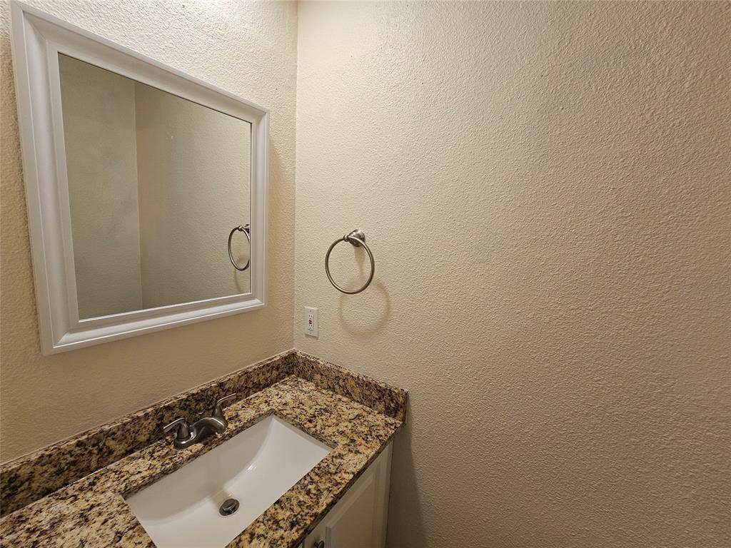 216 Samuel Boulevard, #j3, Coppell, TX 75019 Vanity with an integrated rectangular sink, granite countertop, wall-mounted mirror with a white frame, and brushed nickel fixtures