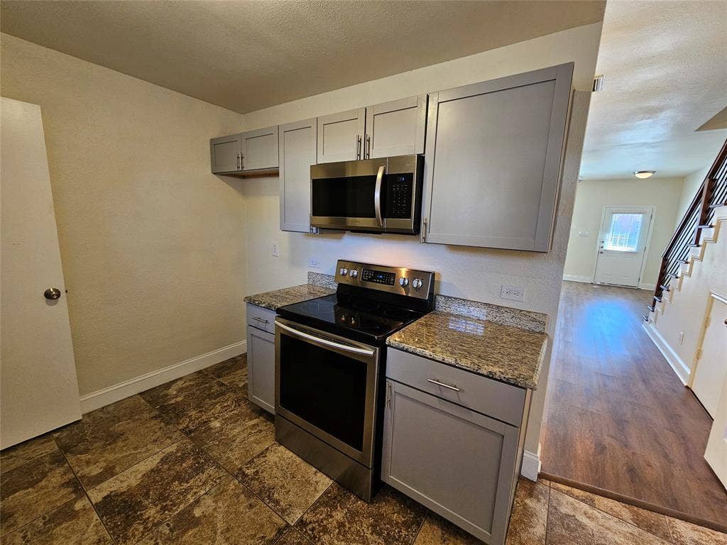 216 Samuel Boulevard, #j3, Coppell, TX 75019 Stainless steel range and microwave, light gray cabinetry, granite countertops, and patterned floor tiles