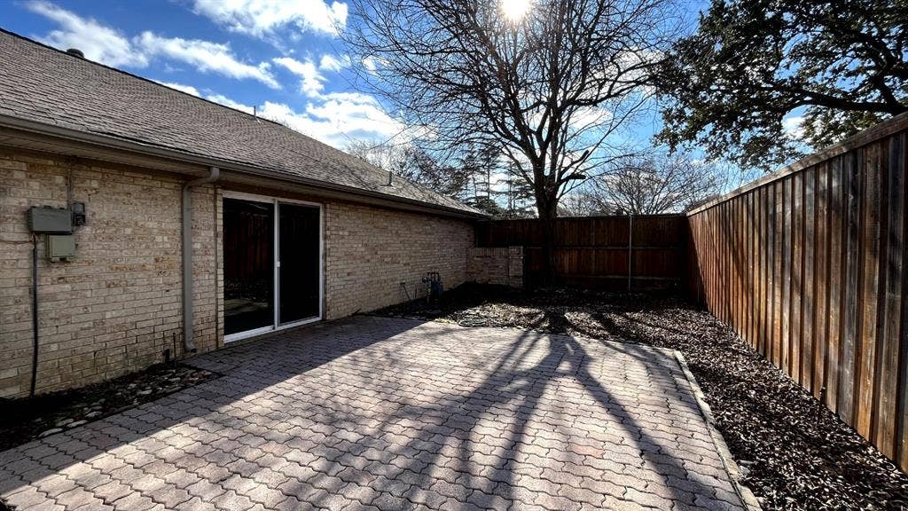 3717 Atrium Drive, Plano, TX 75075 Brick exterior with a paved patio, sliding glass door, and wood privacy fencing