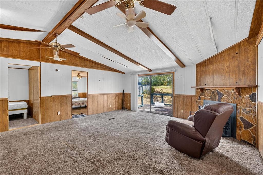 11929-1 County Road 950, Rockwall, TX 75087 Vaulted ceiling with exposed wood beams, stone-faced fireplace, wood paneling, sliding glass door, and ceiling fans