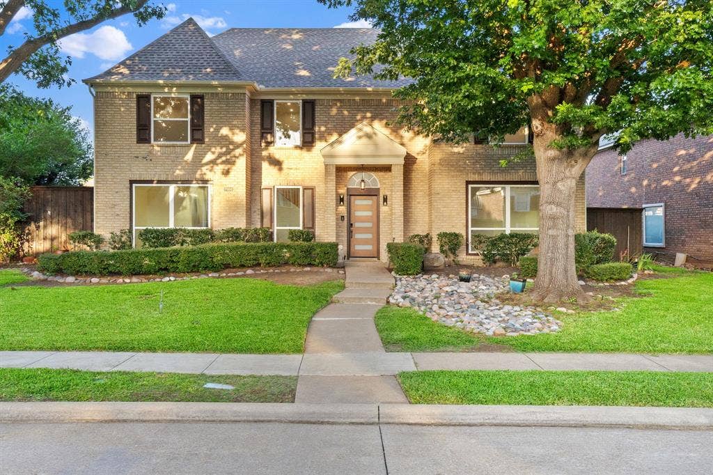 7504 Hughes Drive, Plano, TX 75024 Traditional brick facade residence featuring a prominent entryway, dark-shingle roof, and decorative window shutters