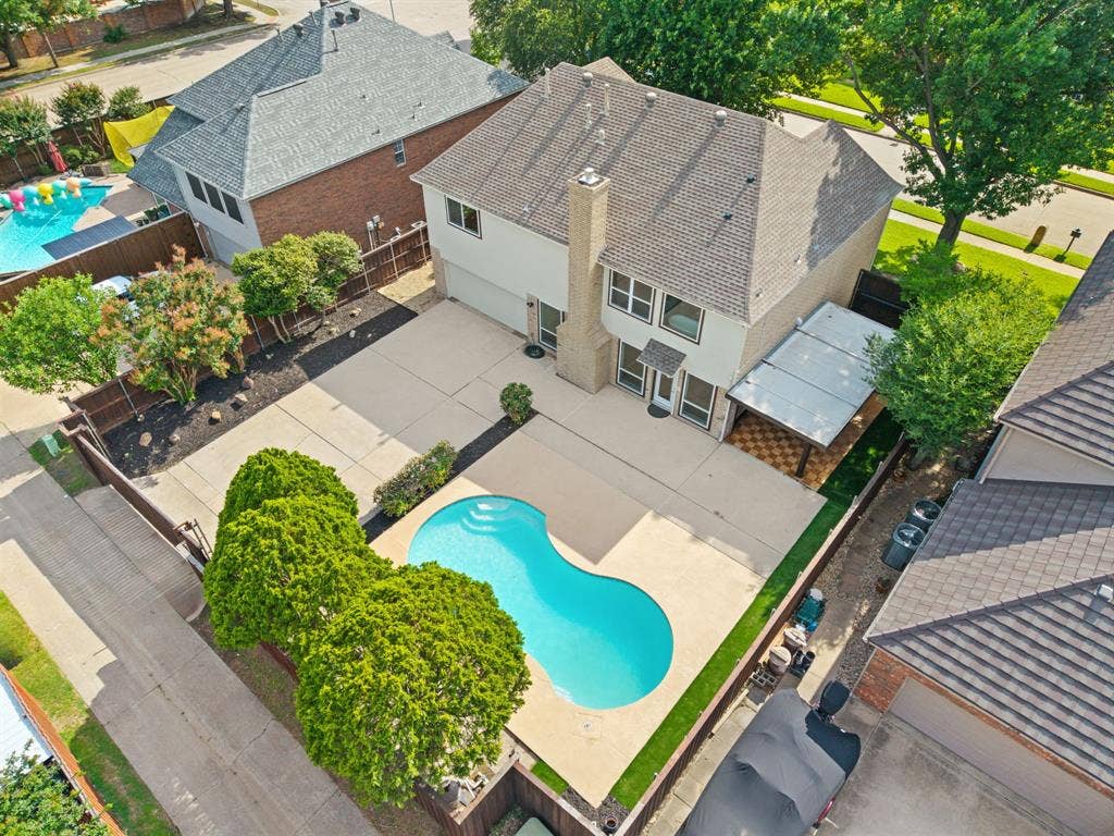 7504 Hughes Drive, Plano, TX 75024 Spacious backyard featuring a kidney-shaped swimming pool, extensive concrete patio, and a covered outdoor living area with patterned tile flooring