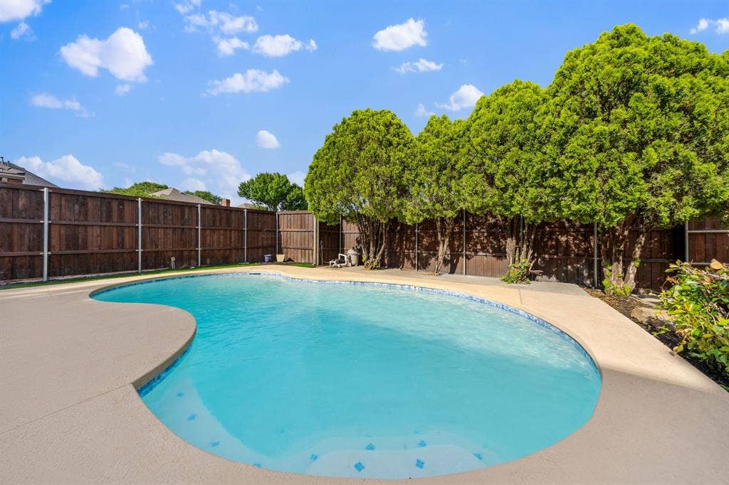 7504 Hughes Drive, Plano, TX 75024 Curved swimming pool featuring a light-colored concrete deck, blue waterline tiling, and a surrounding privacy fence