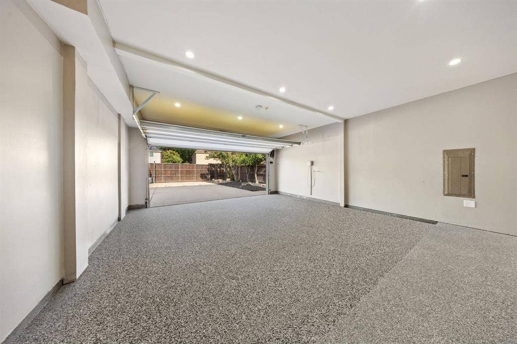 7504 Hughes Drive, Plano, TX 75024 Spacious garage featuring a durable speckled epoxy floor, recessed ceiling lighting, a roll-up door, and painted walls