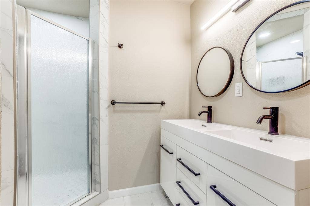 1904 Richland Drive, Richardson, TX 75081 Dual vanity with integrated sinks and matte black fixtures, framed mirrors, and a glass-enclosed shower