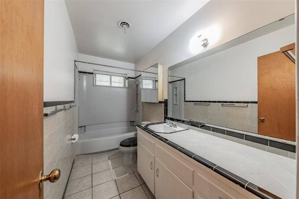 1313 Killian Drive, Arlington, TX 76013 White tile flooring with dark grout, full vanity with integrated sink, expansive wall mirror, built-in medicine cabinet, and a shower-tub combination