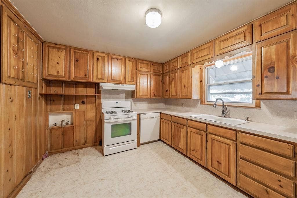 1313 Killian Drive, Arlington, TX 76013 Wood-paneled kitchen featuring extensive cabinetry, white countertops, a double-basin sink with a gooseneck faucet, a white range with an oven, and a white dishwasher